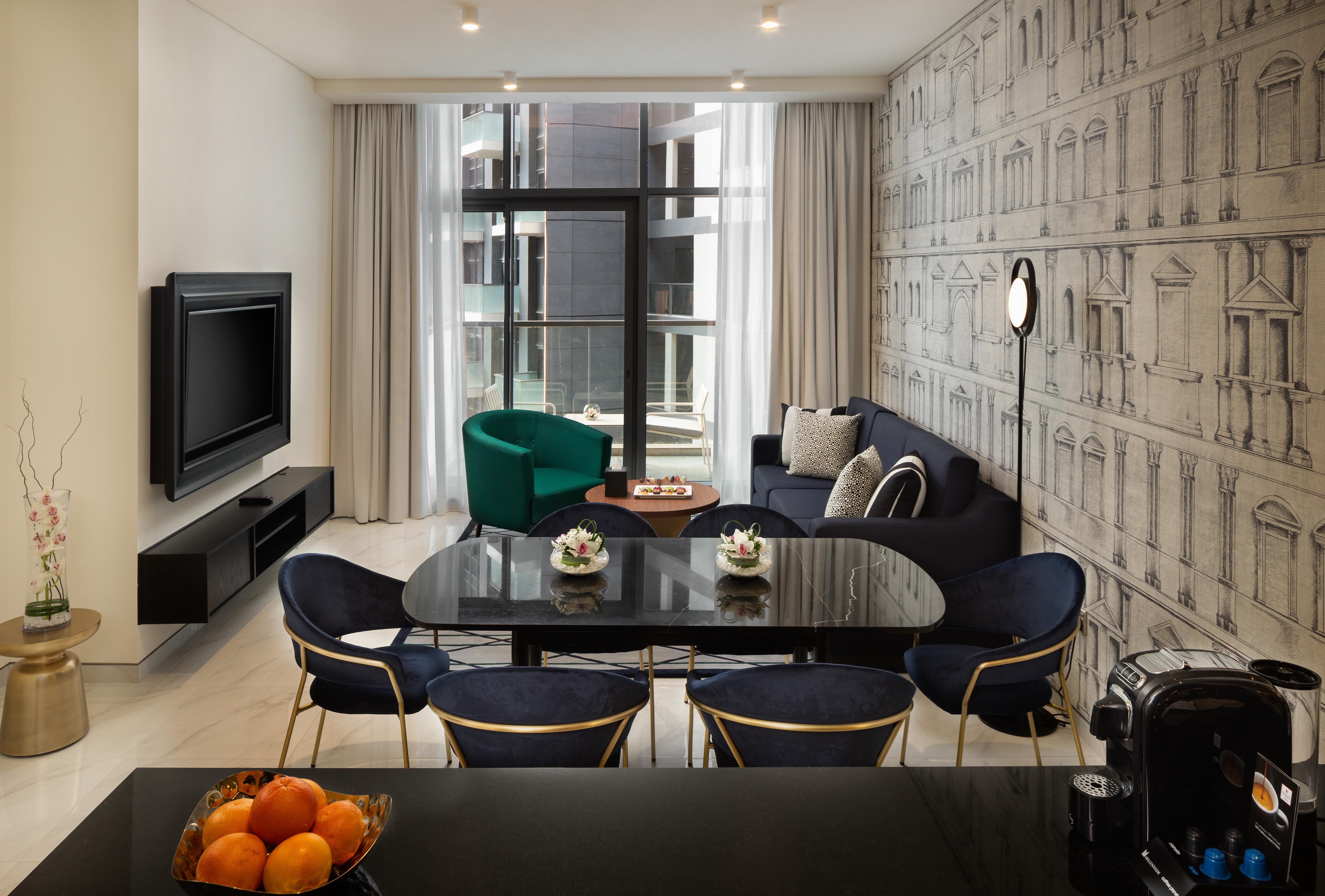 Millennium Atria Business Bay Aparthotel Dubai Bagian luar foto The photo shows a modern living space that includes a cozy seating area and dining setup. On the left, there is a large television mounted on the wall. The living room features a blue sofa and a green accent chair, creating a stylish contrast. A smal