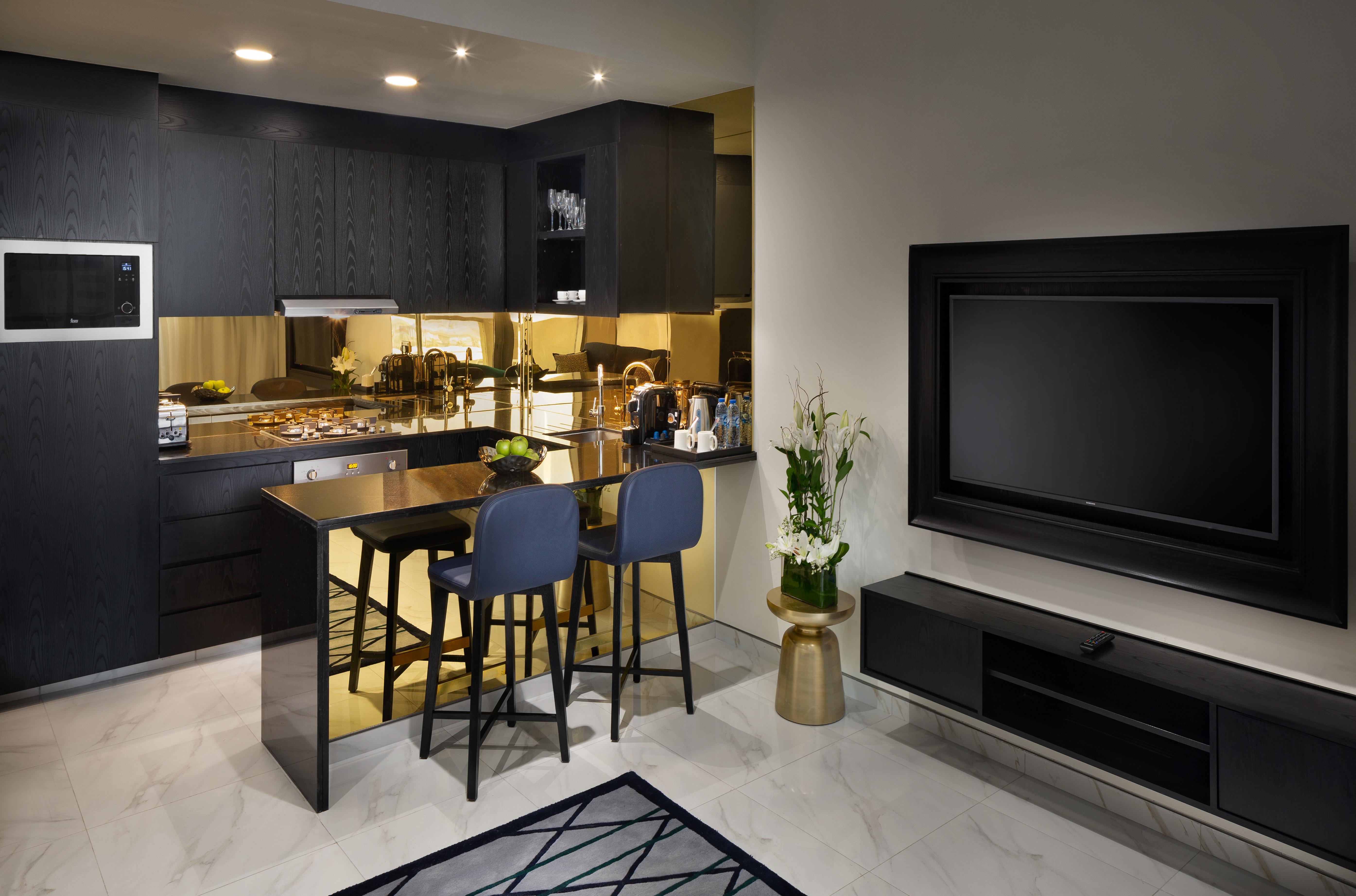 Millennium Atria Business Bay Aparthotel Dubai Bagian luar foto The photo depicts a modern kitchen and living area. The kitchen features dark cabinetry with a clean design, showcasing various appliances, including a stovetop and possibly an oven. There is a kitchen island with two stools, suggesting a space for c