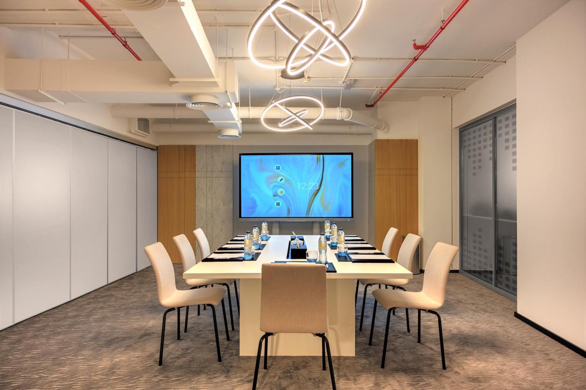 Millennium Atria Business Bay Aparthotel Dubai Bagian luar foto The photo shows a modern conference room designed for meetings. It features a long white table surrounded by beige chairs. At the end of the table, there is a large screen displaying a blue abstract design. The room is well-lit with contemporary ligh