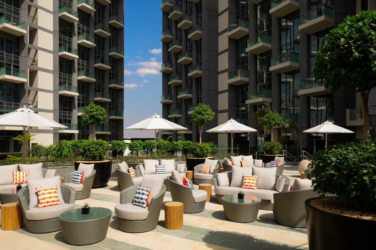 Millennium Atria Business Bay Aparthotel Dubai Bagian luar foto The photo shows a modern outdoor lounge area, featuring several comfortable seating arrangements made of soft, stylish lounge chairs and round tables. The seating is adorned with colorful pillows, adding a pop of color to the neutral tones of the fur