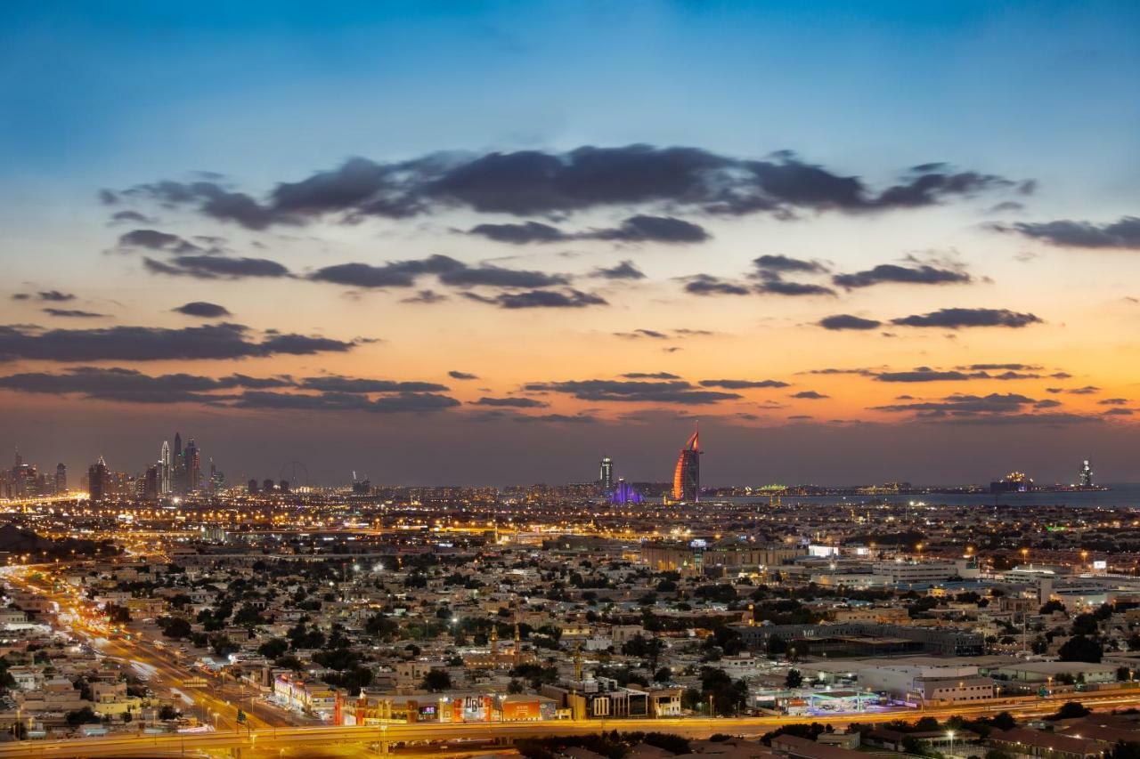 Millennium Atria Business Bay Aparthotel Dubai Bagian luar foto The photo shows a stunning cityscape at dusk, with a panoramic view of a city skyline. The sky is transitioning from blue to orange, indicating sunset, with scattered clouds creating a colorful backdrop. In the foreground, you can see a sprawling urb