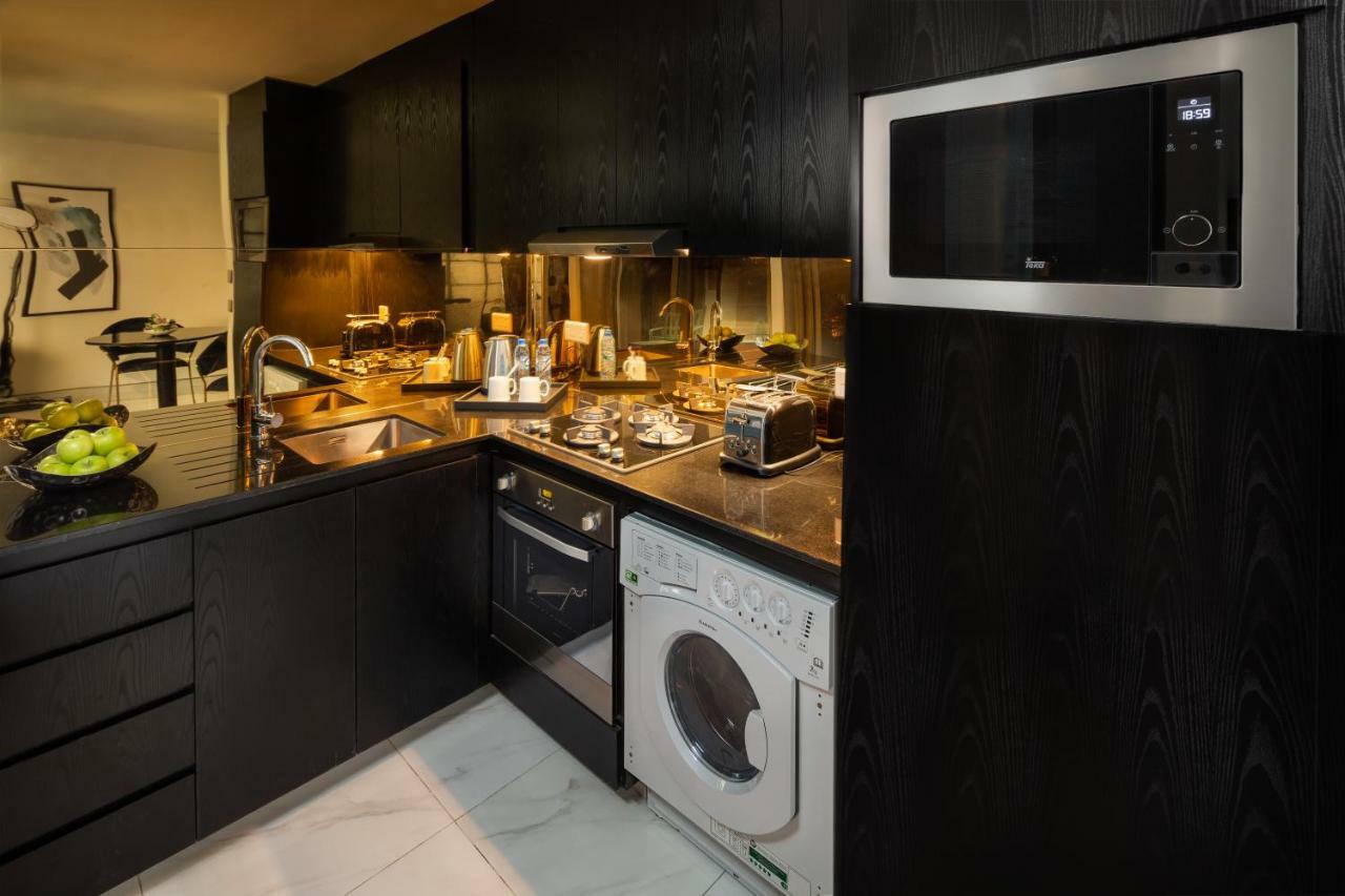 Millennium Atria Business Bay Aparthotel Dubai Bagian luar foto The photo shows a modern kitchen with a sleek design. The cabinets and surfaces are predominantly black, creating a contemporary look. There is a stainless steel microwave mounted above the countertop, and on the counter, various kitchen appliances l